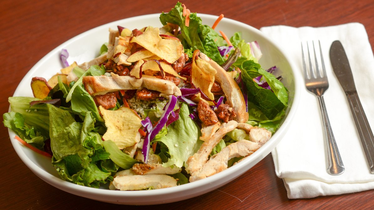 A salad with chicken, lettuce, and chips on a wooden table.