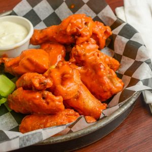 Buffalo wings on a plate with a side of dipping sauce.
