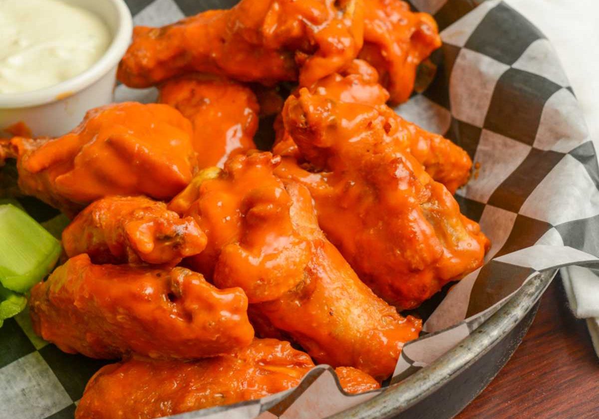 Buffalo wings on a plate with a side of dipping sauce.